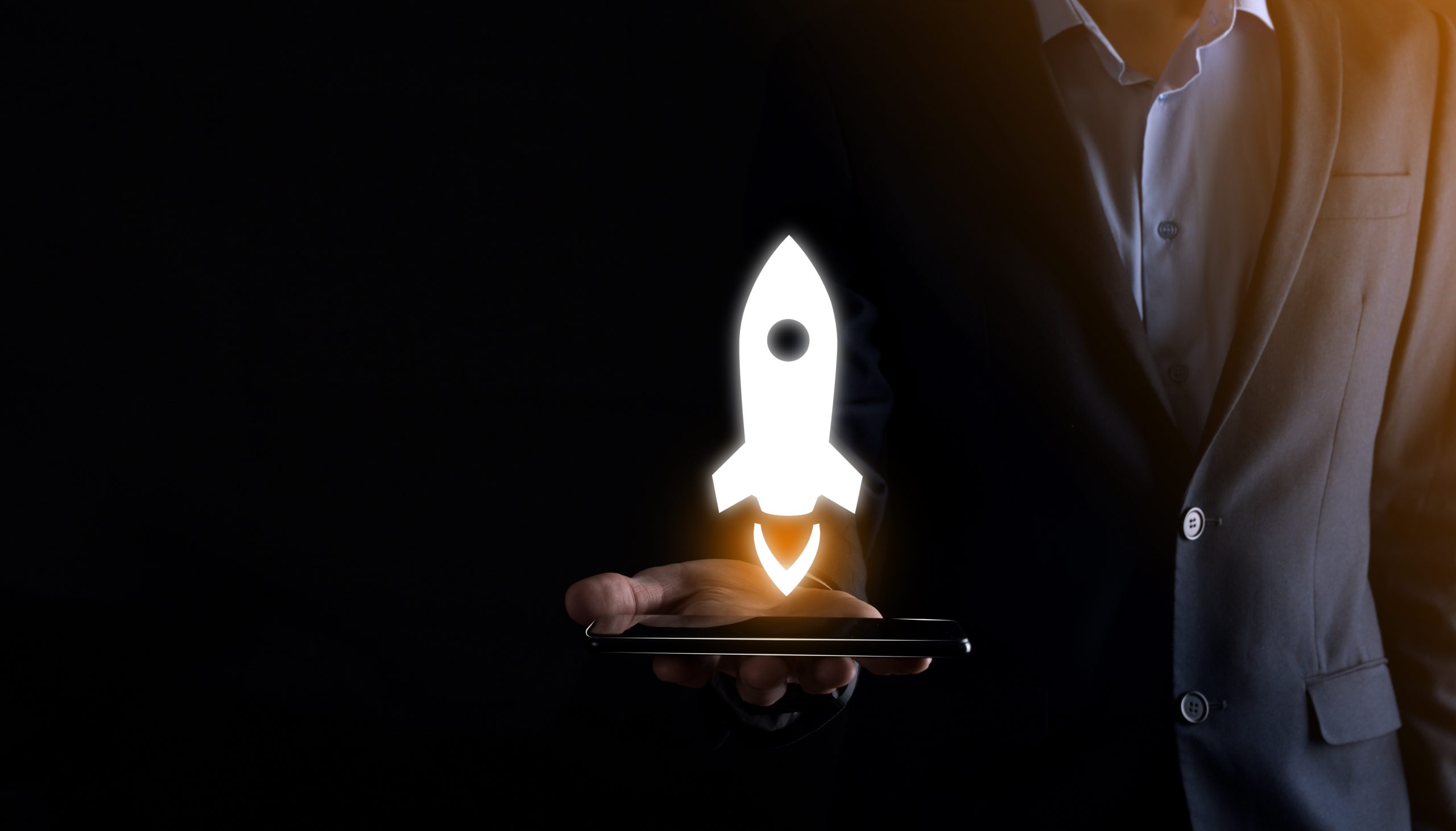 Startup business concept, Businessman holding tablet and icon rocket is launching and soar flying out from screen with network connection on dark background.